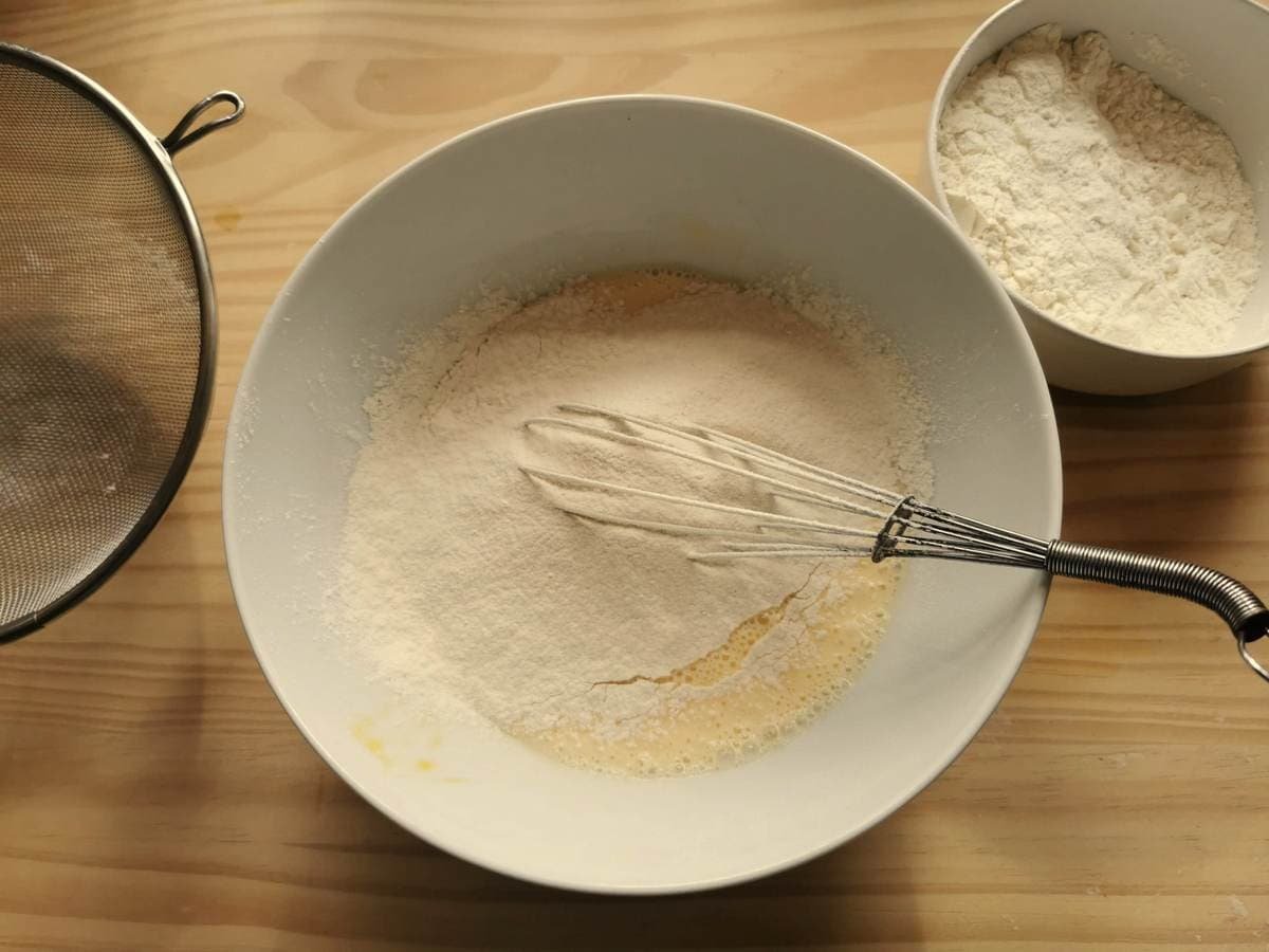 White flour added to the bowl with beaten egg and milk.