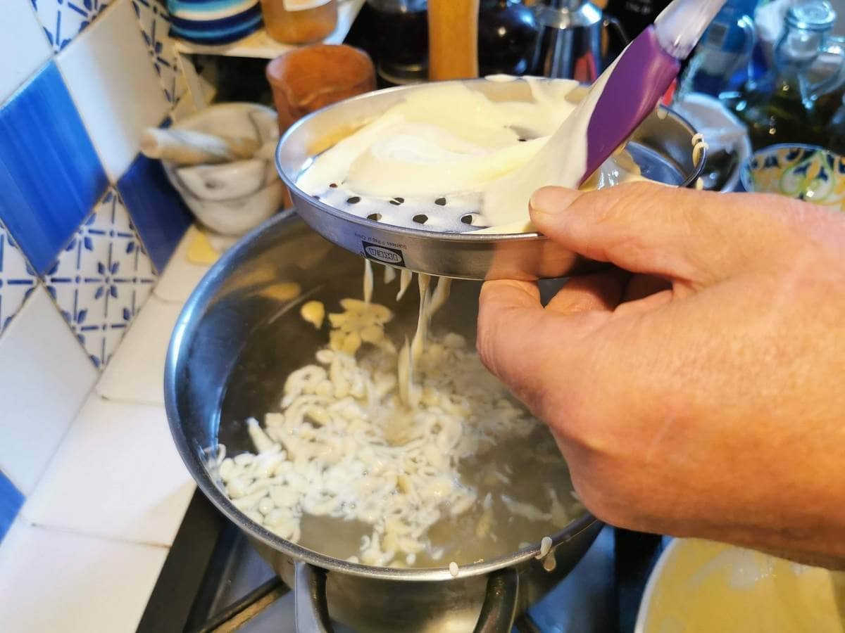 The Chnèfflènè dough is pushed through a grater and dropped into a pot of boiling salted water.