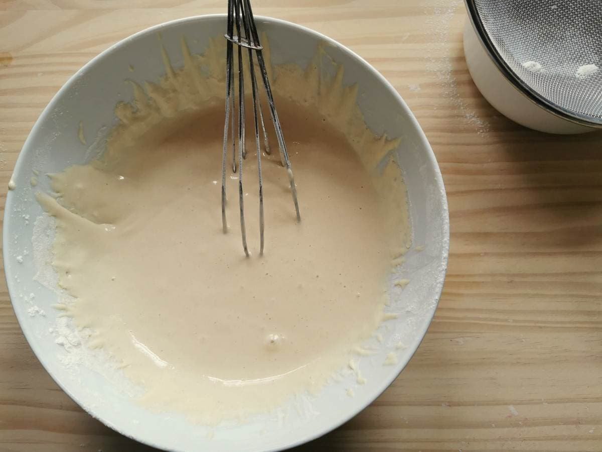 Dough for Italian drop balls (chnèfflènè) in white bowl with whisk.