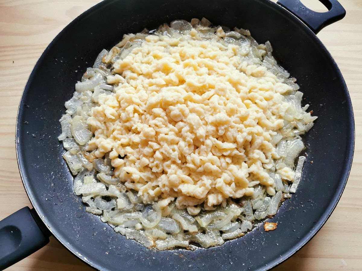 Ready-cooked Italian dumplings (chnèfflènè) in a frying pan with cooked onions.