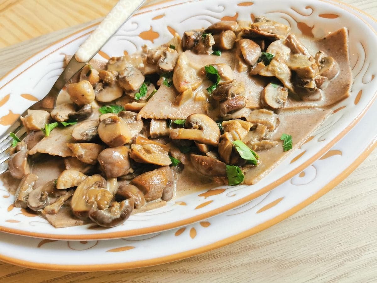 Chestnut flour maltagliati pasta from Lombardy with mushroom sauce in a white and orange oval dish.