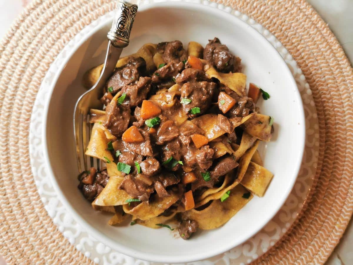 Braised hare ragu with pappardelle in a white bowl.