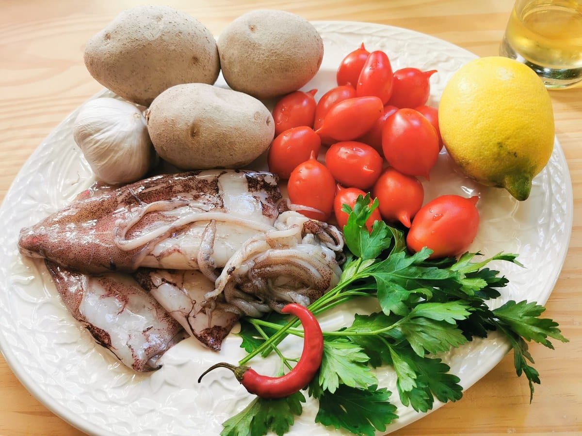 Octopus, potatoes, garlic, cherry tomatoes, chilli, lemon and white wine on a kitchen table.