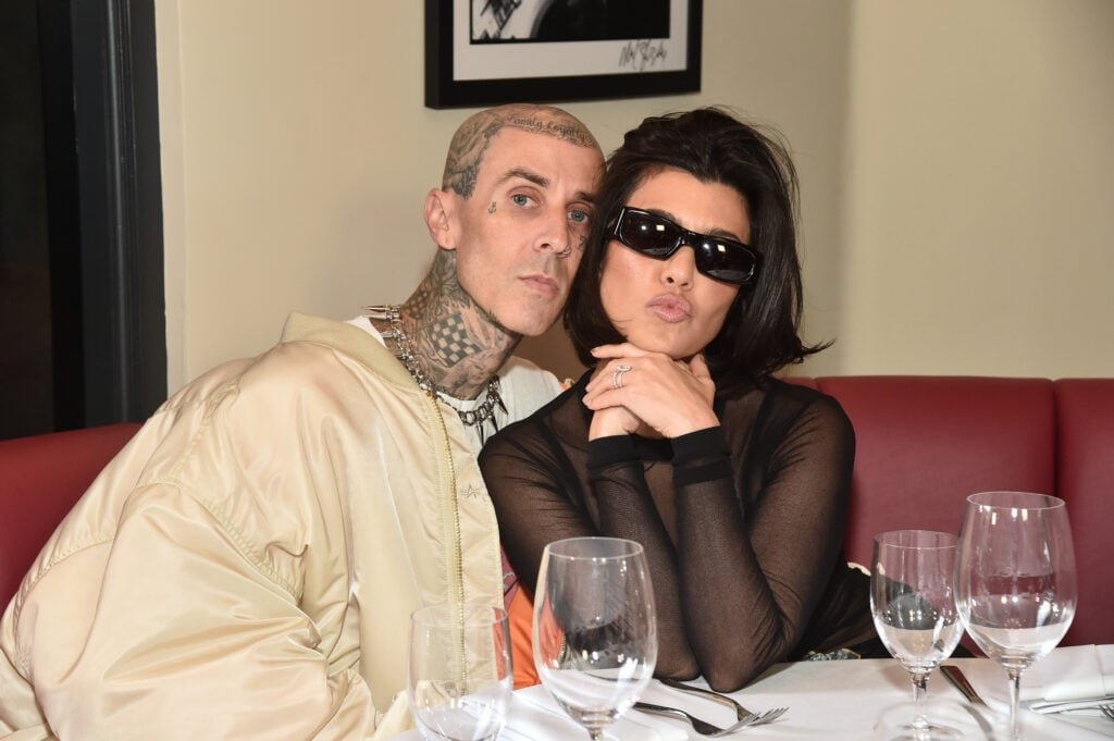 Travis Barker and Kourtney Kardashian posing for a photo while eating at a restaurant.