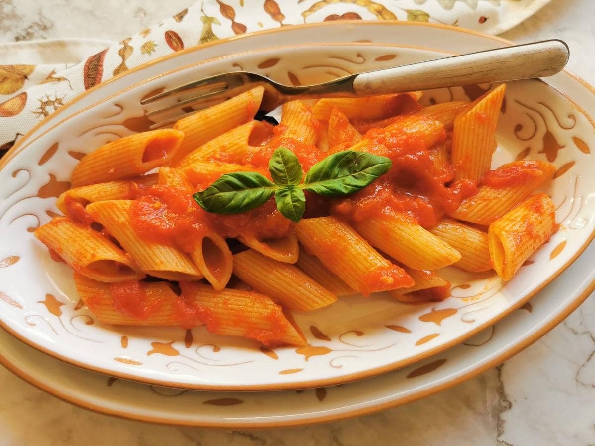 Penne Pomodoro in white and terracotta serving bowl with fork.