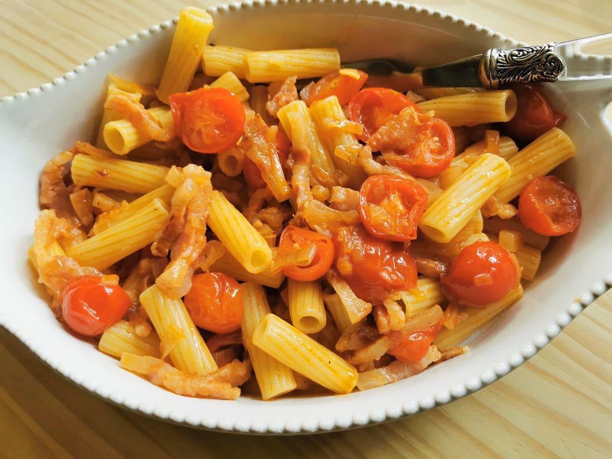 Rigatoni Pasta with shallots and guancial in white serving bowl.