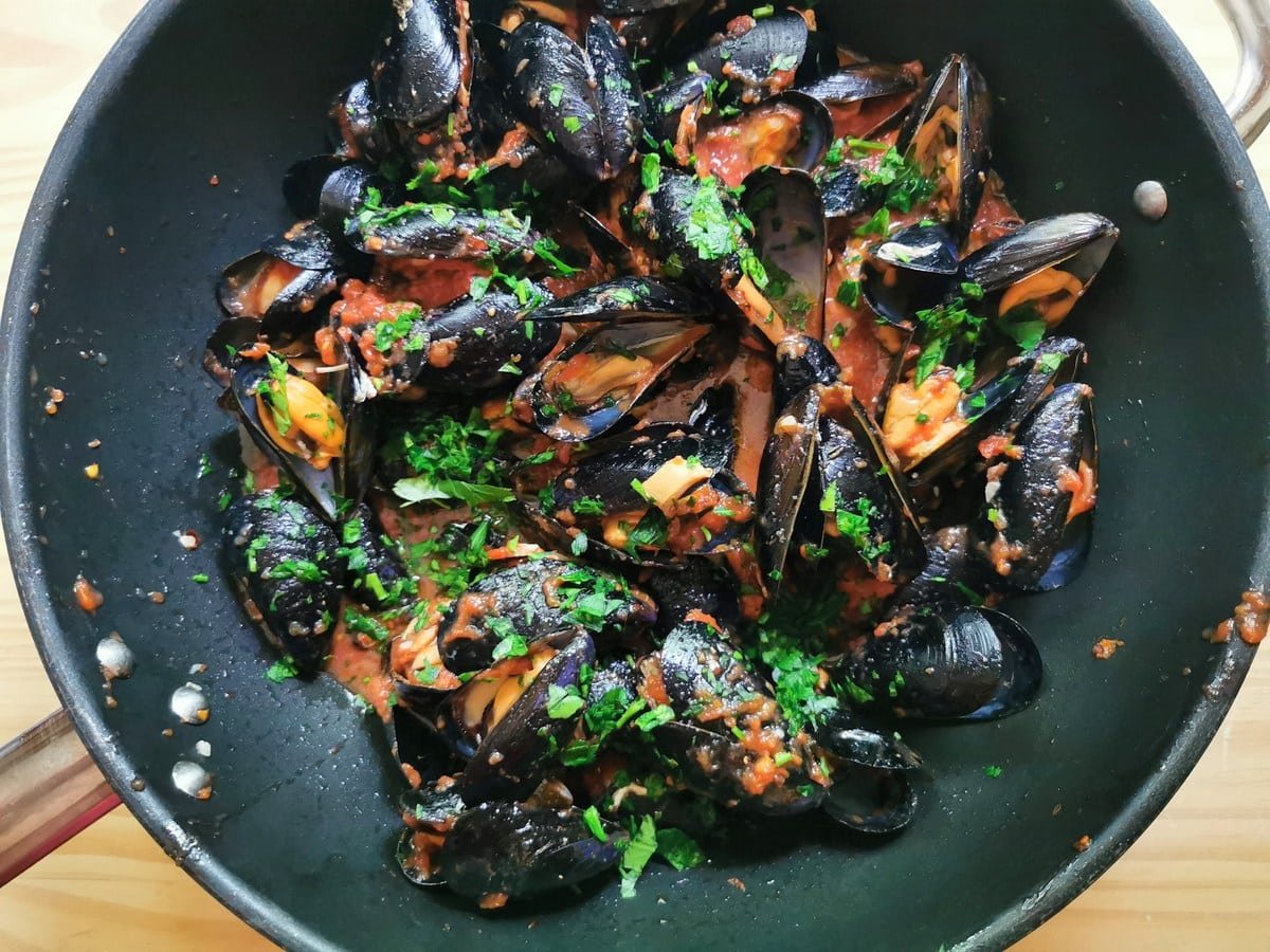 Cooked mussels in tomato sauce with chopped parsley sprinkled on top.