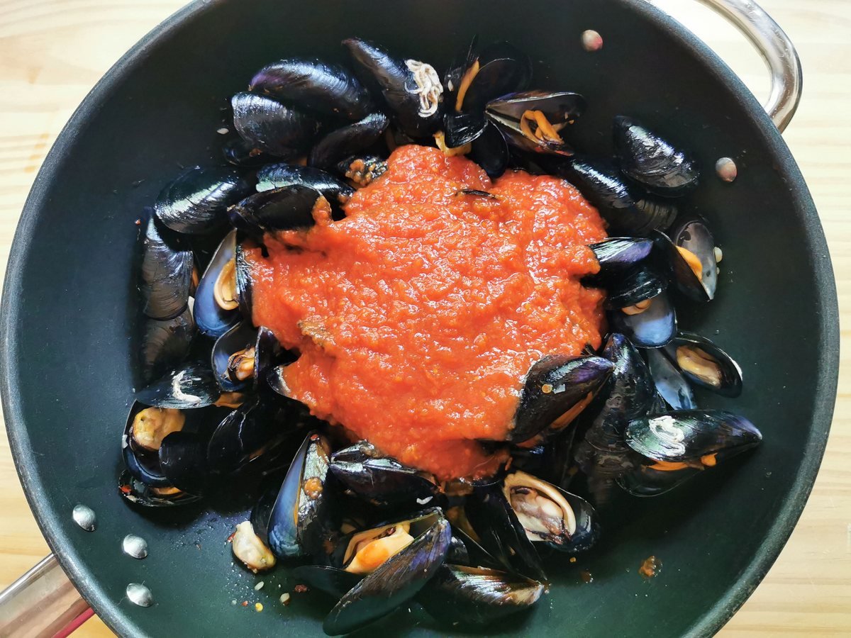 Cooked mussels in large frying pan with added tomato passport.