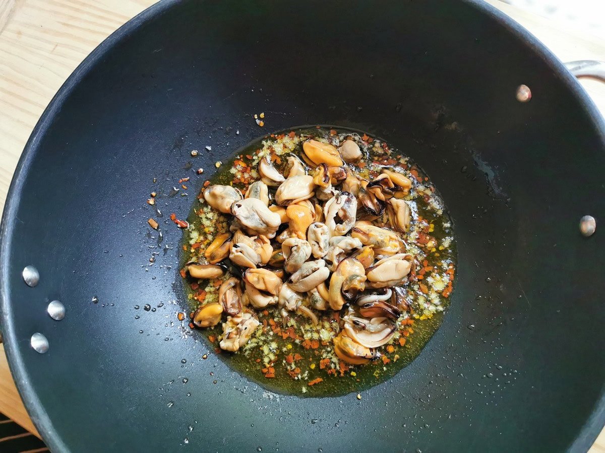 Chopped garlic, red pepper flakes and peeled clams cooking in olive oil in large frying pan.